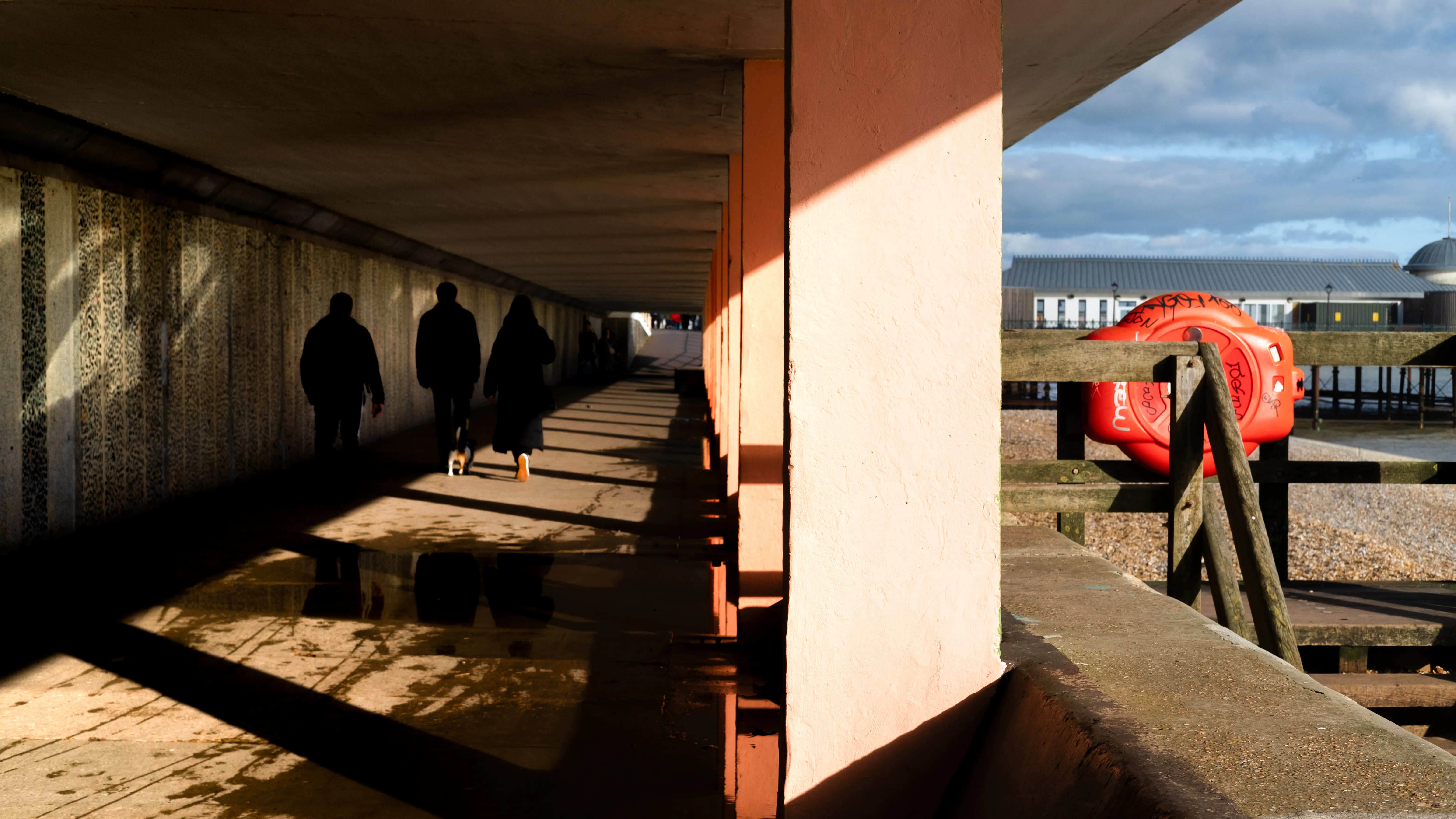 Silhouettes of walkers in an underpass along the seafront, warm evening light