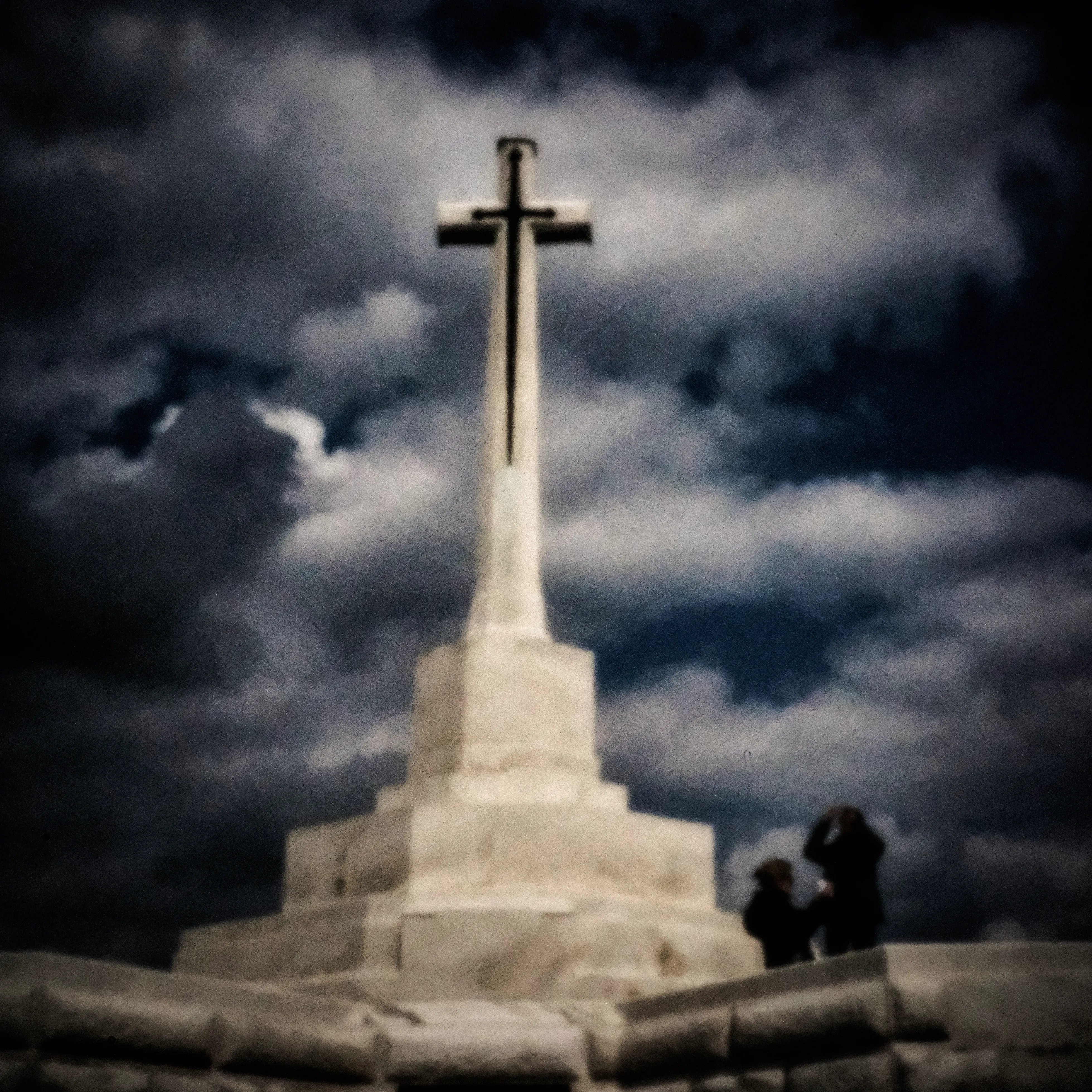 Wit oorlogsmonument met kruis onder een dreigende wolkenlucht bij Ieper