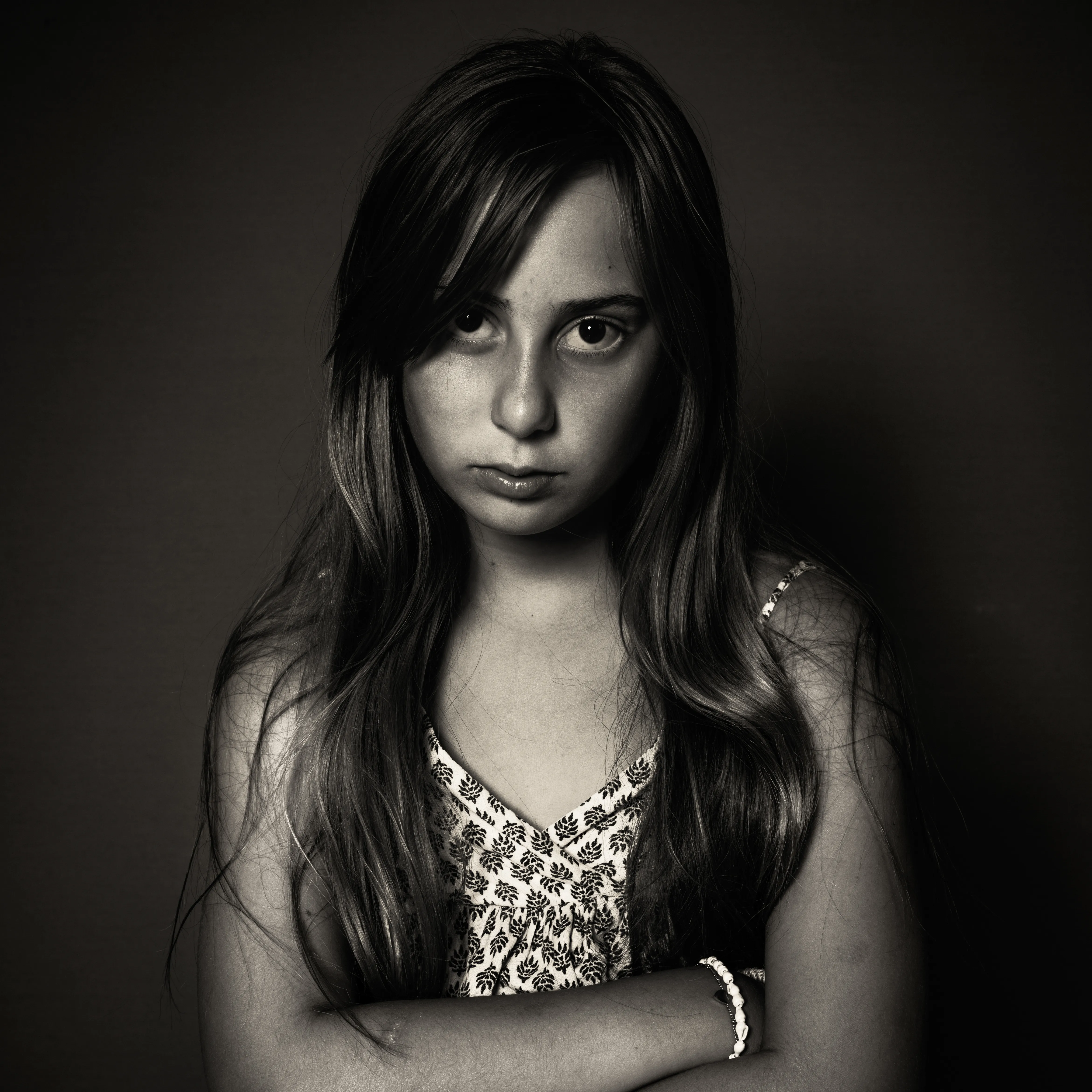 Portret van een meisje met lang haar en gekruiste armen, tegen een donkere achtergrond