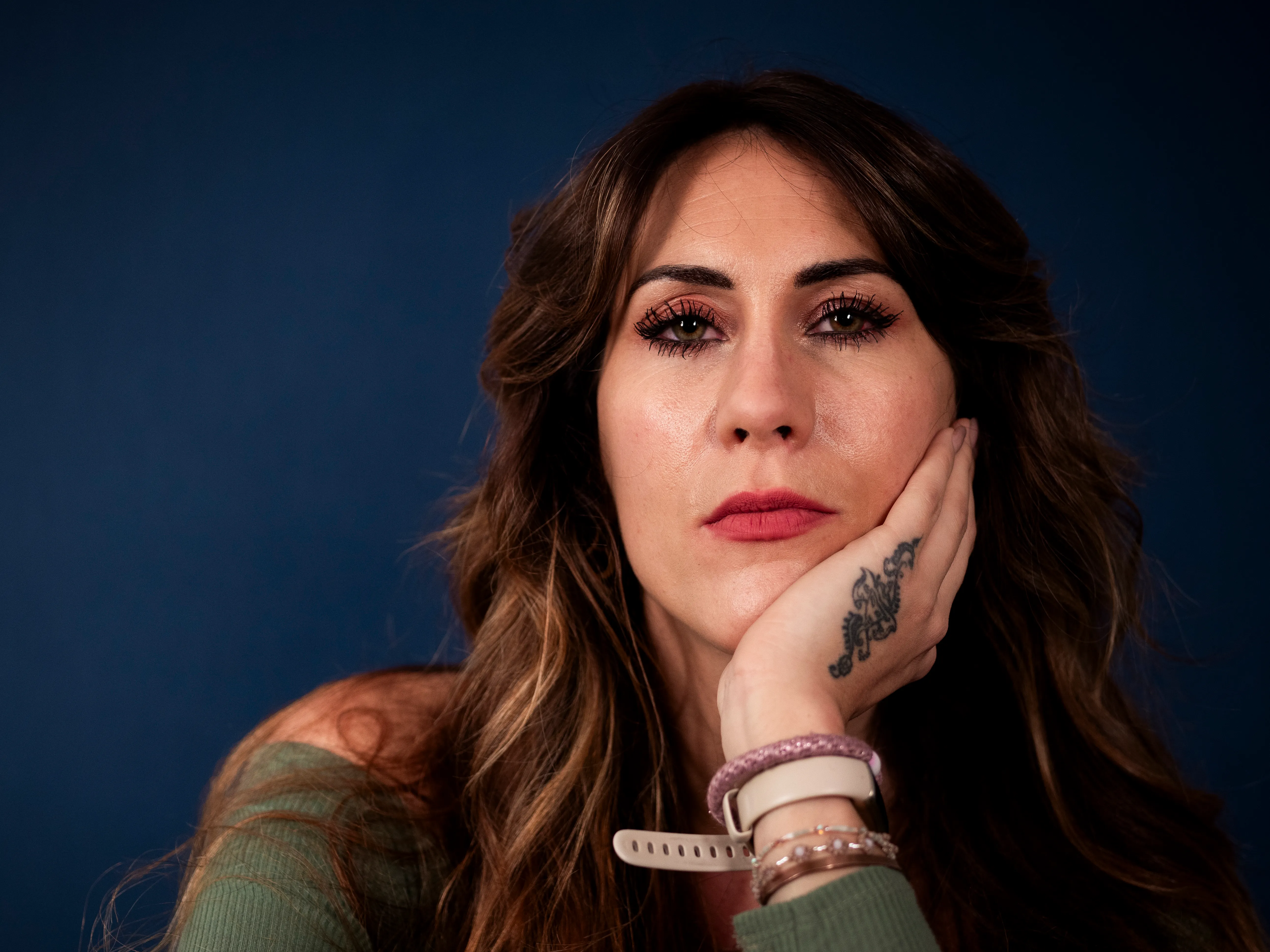 Kleurenportret van een vrouw met tatoeage, hand tegen de wang, tegen een blauwe achtergrond