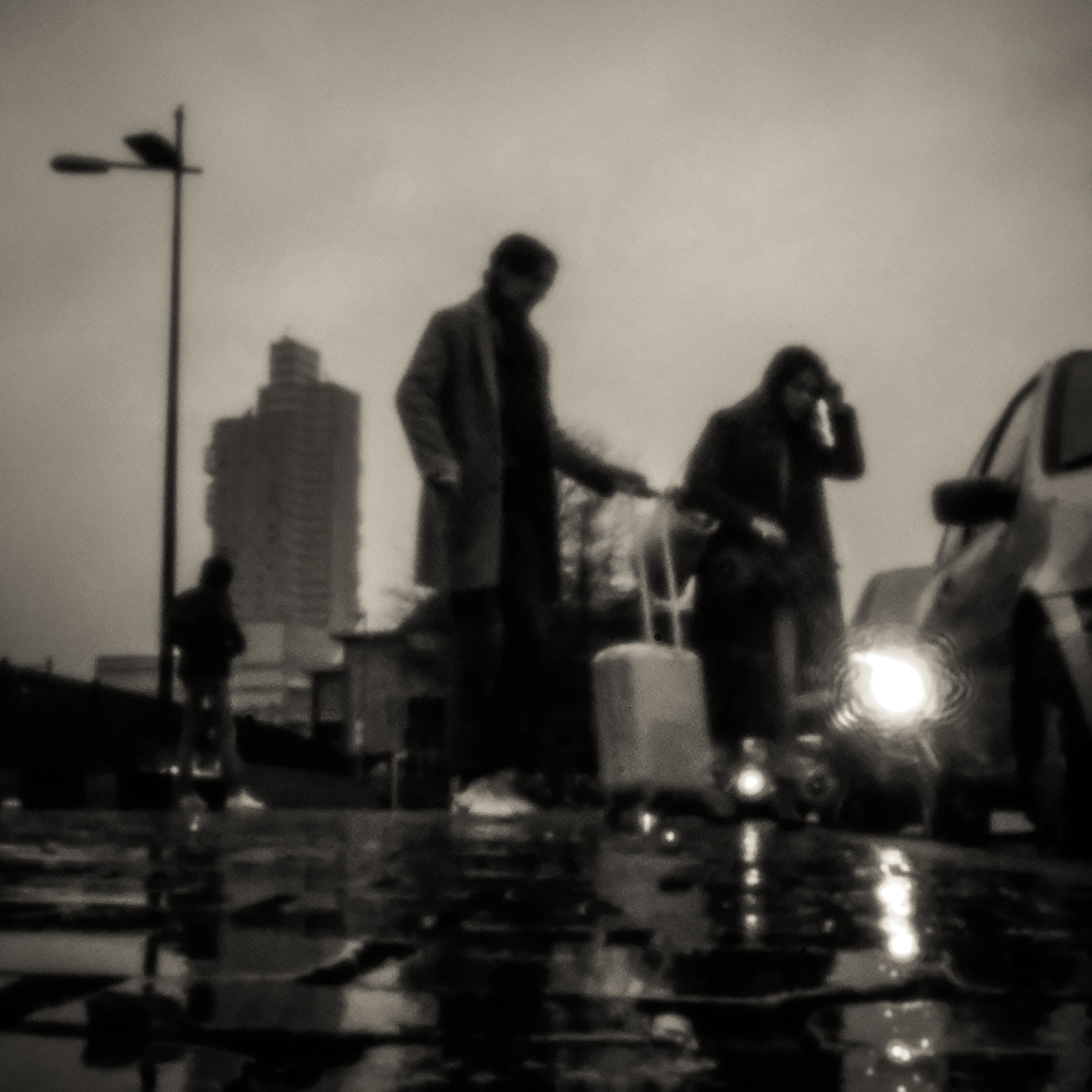 Travellers with suitcases on a wet square, blurred by the long exposure