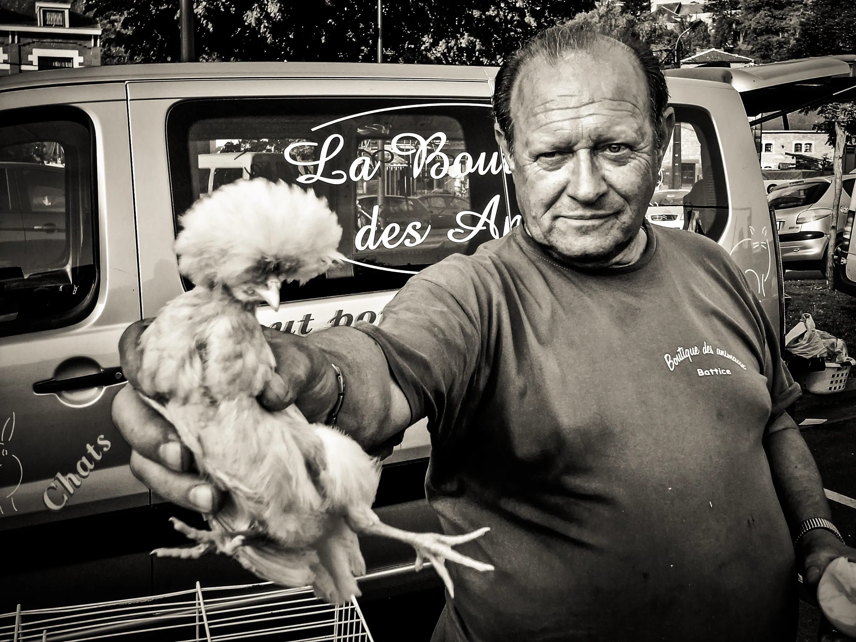 Man at a market in Esneux laughing as he holds up a white chicken